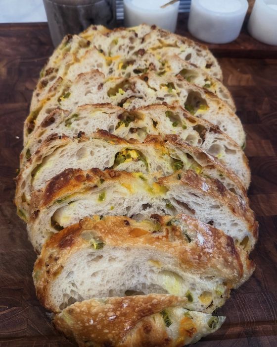 Sliced cheddar jalapeño sourdough loaf on a walnut board, open crumb with melted cheddar and green jalapeño
